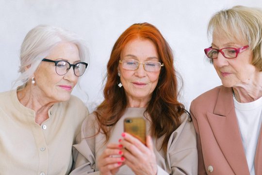 Group of elderly fashionable elegant women surfing internet on mobile phone together